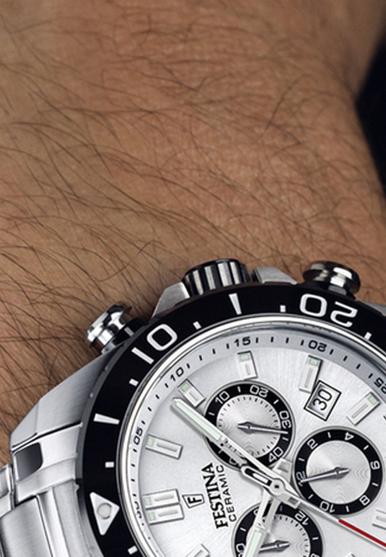 Montre chronographe argentée avec une lunette noire, un bracelet en acier inoxydable et un cadran texturé présentant plusieurs sous-cadrans et des index horaires lumineux.