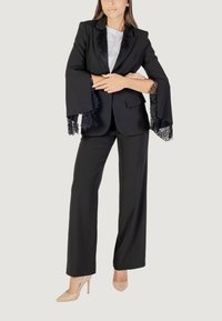 Completo nero con bordo in pizzo sulle maniche, vestibilità sartoriale, pantaloni plissettati e tacchi beige in abbinamento. L'outfit presenta un top in satin sotto la giacca.