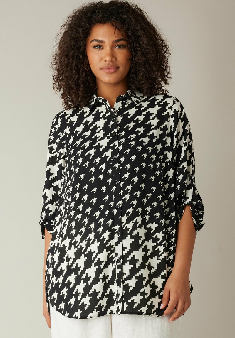 Camisa de botones de patrón de espiga en blanco y negro, con cuello, mangas enrollables y un corte relajado, fabricada en tela suave.