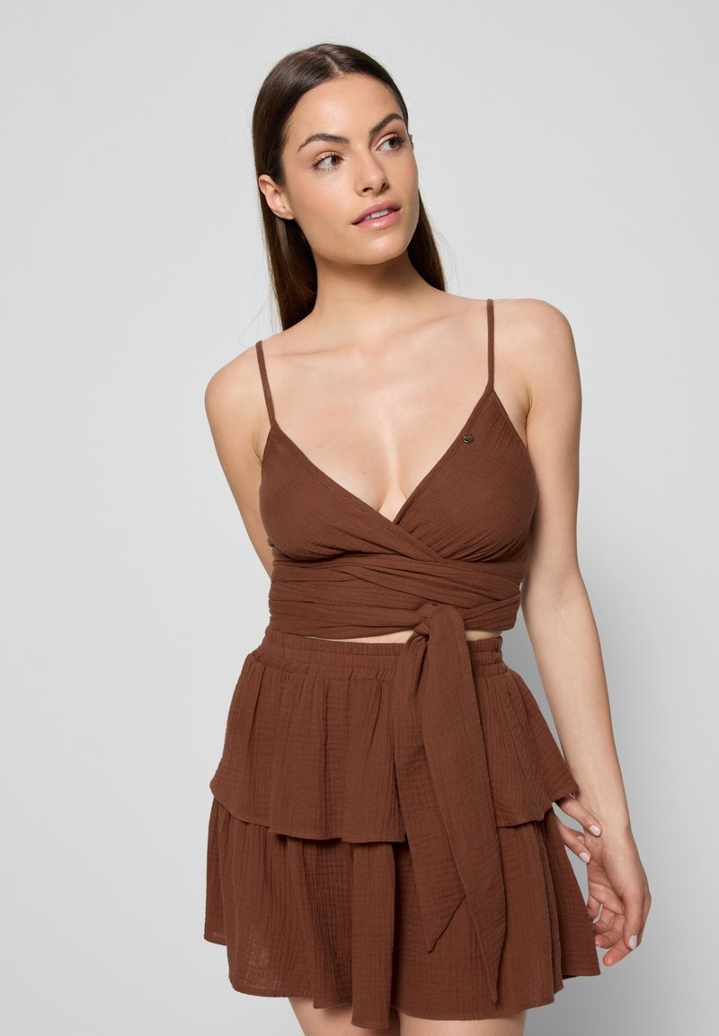 Bruine wikkeltop met dunne bandjes en gestructureerde stof, gecombineerd met een bijpassende gelaagde minirok met een strikdetail in de taille.