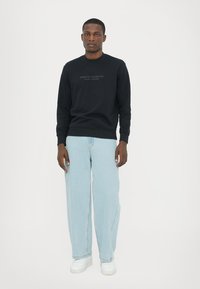 Marineblauwe sweatshirt met ronde hals en tonale logo. Gepaarde met lichtblauwe wijde jeans en witte sneakers. Eenvoudige, casual uitstraling.