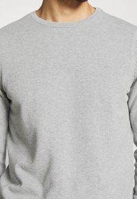 Szary sweter z długim rękawem i okrągłym dekoltem, wykonany z miękkiej, teksturowanej tkaniny. Posiada prążkowany dekolt i dopasowane rękawy, zakończony gładkim wykończeniem.