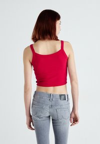Top curto canelado vermelho com alças finas, combinado com jeans justos cinzas. O top tem um decote arredondado e uma barra que fica acima da cintura.
