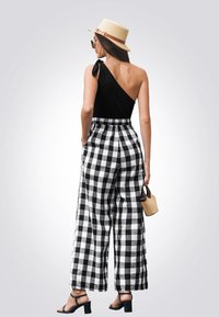 Top negro de un solo hombro combinado con pantalones de cuadros en blanco y negro de pierna ancha. El atuendo incluye un sombrero de paja y sandalias negras de tacón cuadrado.