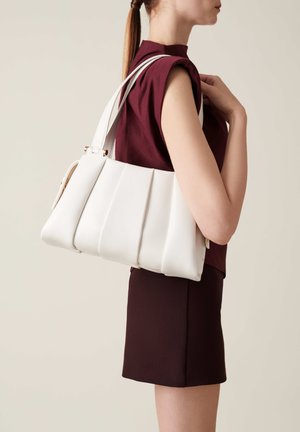 Borsa bianca a pieghe con doppie cinghie, caratterizzata da una texture liscia e sottili accenti dorati, indossata sulla spalla con un top amaranto.