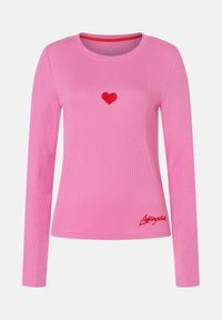 Rosa langärmeliges Ripphemd mit rotem gesticktem Herzen in der Mitte der Brust und rotem, kursive Text nahe dem unteren Saum auf einem einfarbigen Hintergrund.