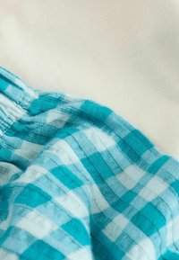 Sinine ja valge ruuduline kangas nähtavate õmblustega naastuvalge ühevärvilise kangaga, mõlemad esitatud lähivõttes.