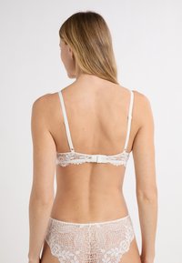 White lace bralette with adjustable straps, featuring floral patterns and a hook-and-eye back closure. Delicate, semi-sheer texture.