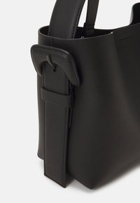 Czarna skórzana torebka o usztywnionej konstrukcji, z uchwytem u góry i wyraźnym paskiem jako detalem. Gładka faktura i minimalistyczny styl.