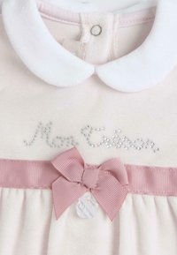 Svetle růžové šaty s bílým límečkem, "Mon Câlin" ve stříbrných flitrech, mají růžovou stuhu a mašli v pase, měkká texturovaná látka.