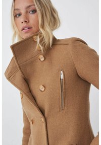 Abrigo de mezcla de lana marrón con botones de doble botonadura, cuello alto y un bolsillo con cremallera lateral. Tejido texturizado con un corte entallado y un diseño estructurado.
