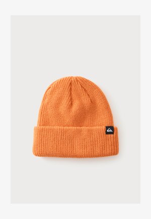 Orange ribstrikket hue med opbrettet kant og lille sort rektangulært logo-patch på kanten mod en ensfarvet baggrund.