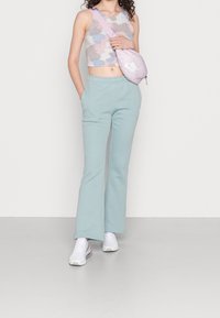 Světlé modré tepláky s volným střihem a bočními kapsami, doplněné o vícebarevný crop top a malou růžovou tašku na rameno značky Nike.