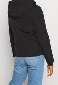 Svart vadderad jacka med huva, med en slät textur och figursydd midja, kombinerad med ljusblå högmidjade jeans.
