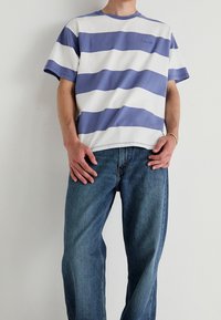 Randig t-shirt i lavendel och vit bomull med korta ärmar, i kombination med blekta blå raka jeans. Minimal design.