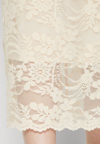 Blonde skjørt med blomster mønster i kremfarge, med en bølget kant og teksturert, gjennomsiktig stoff. Elegant, delikat design.