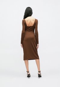 Καφ έ φόρεμα μακρυμάνικο με στρογγυλή πλάτη και εφαρμοστή σχεδίαση, κατασκευασμένο από λείο ύφασμα, μήκους μέχρι το γόνατο, σε συνδυασμό με μαύρα τακούνια με λουράκι στον αστράγαλο.