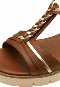 Sandal in pelle marrone con un accento intrecciato dorato, caratterizzato da un design a fascia larga e una suola beige texture.