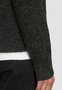 Donkergrijze gebreide trui met een geribbelde textuur, lange mouwen en een iets verkorte zoom. Draag over een wit T-shirt.