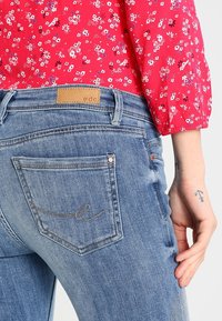 Jeans de mezclilla azul con una altura de cintura media, que presentan una etiqueta de cuero con la inscripción "edc" y costuras decorativas en el bolsillo trasero.