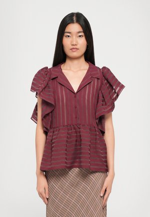 Maroon peplum blouse with ruffled sleeves, vertical stripes, and a button-down front. Worn with a patterned skirt. Smooth texture.