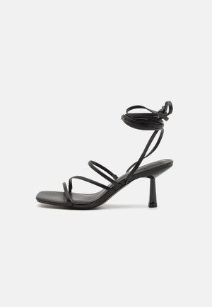 Sandalia negra de tiras con punta cuadrada, lazos ajustables en el tobillo y un tacón bloque delgado. Fabricada con un material suave y duradero.