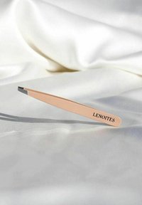 Pincett med ett ljusrosa handtag och silverfärgad spets som vilar på vit satin, med varumärket "LENOITES" tryckt på handtaget.