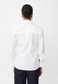 Camisa blanca de manga larga con cuello puntiagudo, puños abotonados y textura suave, combinada con pantalones de mezclilla oscura.
