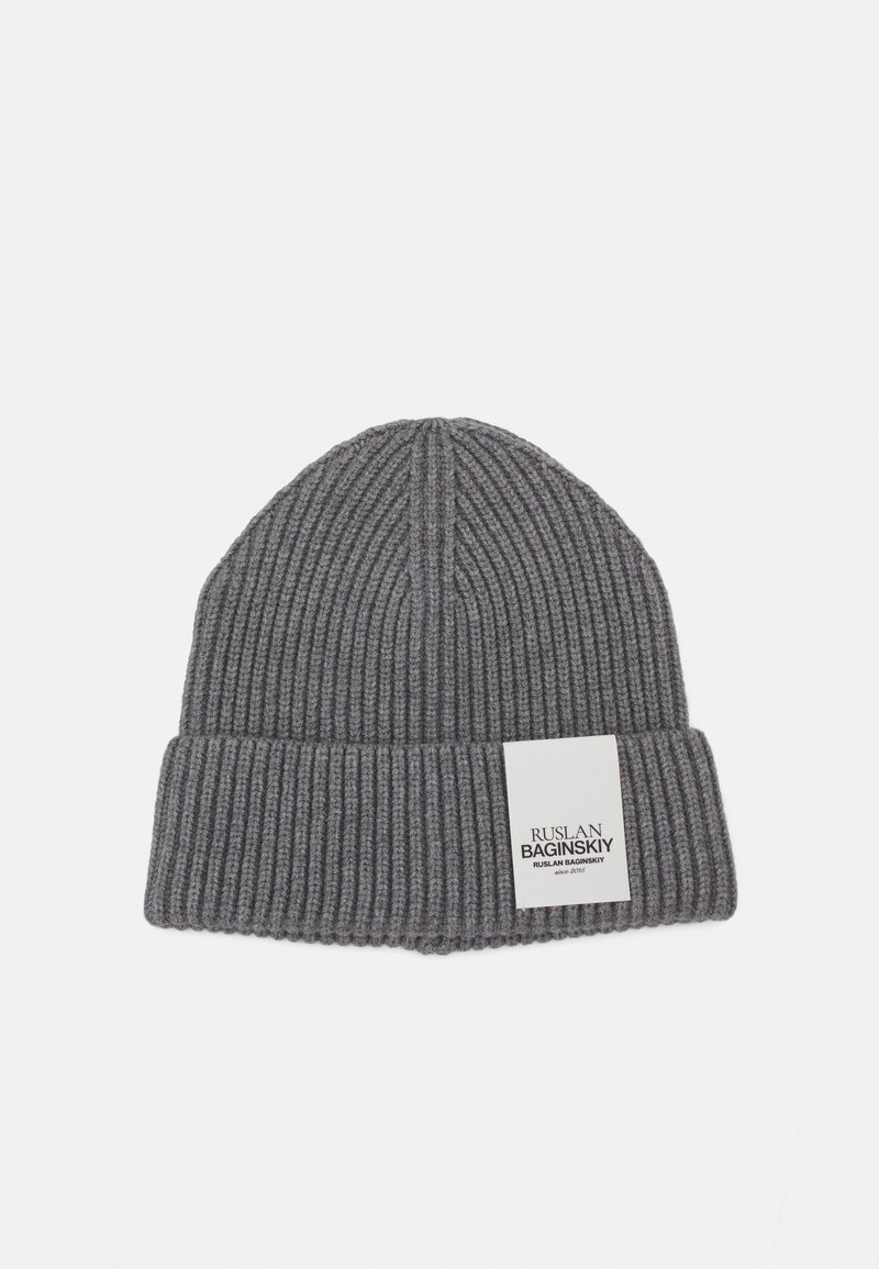 Bonnet gris à côtes avec un revers et une étiquette blanche comportant du texte noir. Fabriqué en matériau tricoté doux, avec une surface texturée.