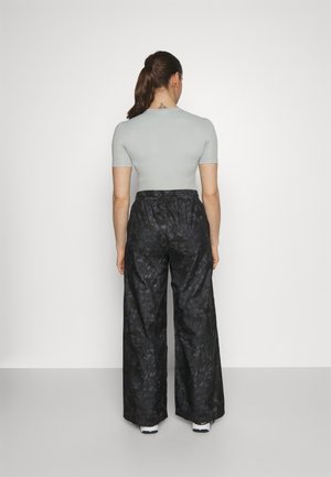 Femme avec une queue de cheval, vue de dos, portant un haut gris clair à manches courtes et un pantalon noir taille haute à jambes larges avec un motif subtil.