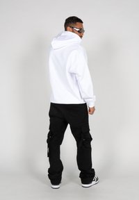 Witte hoodie gemaakt van dik materiaal, gecombineerd met zwarte cargobroeken met zakken en een relaxte pasvorm, gedragen met zwarte zonnebril.