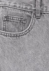 Tissu en denim gris avec une poche avant, une texture subtile, des rivets métalliques et des détails de couture visibles le long des bords.