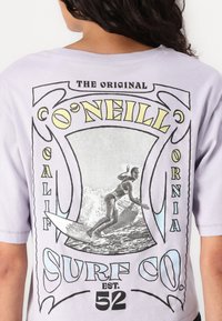 Fialové oversized tričko s grafickým potlačou surferu, s čiernym a žltým textom "O'Neill" a "Surf Co." na zadnej strane.