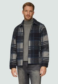 Karierte Wollmischung Jacke in Marineblau, Grau und Blau. Mit Kragen, Reißverschluss vorne und Seitentaschen. Getragen über einem grauen Rollkragenpullover.