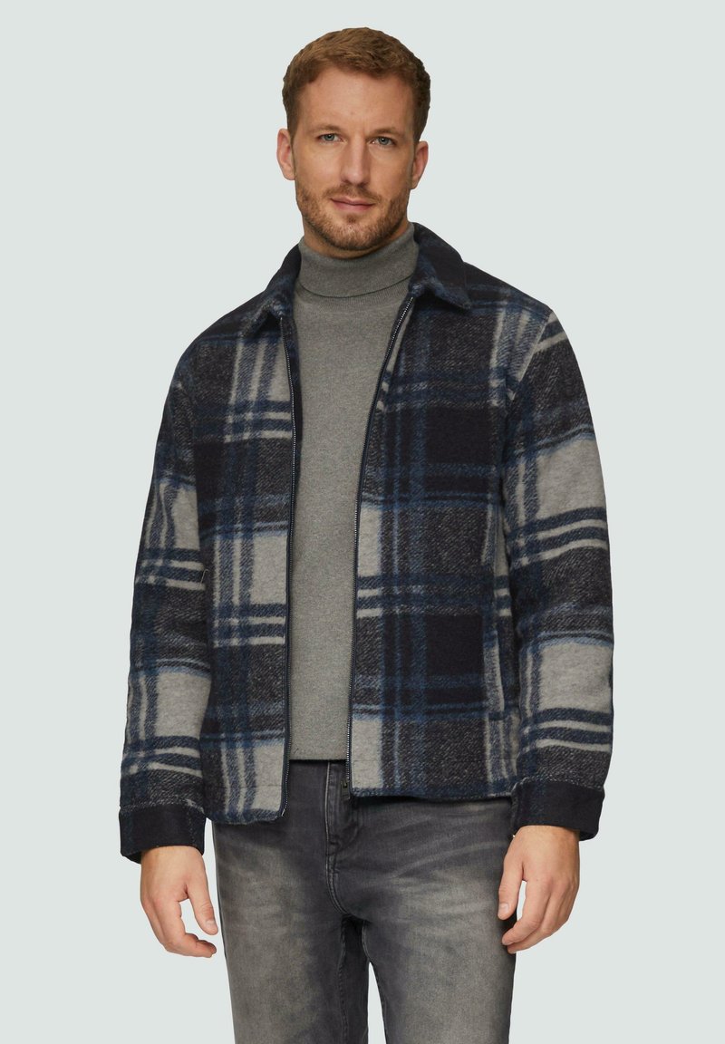 Karierte Wollmischung Jacke in Marineblau, Grau und Blau. Mit Kragen, Reißverschluss vorne und Seitentaschen. Getragen über einem grauen Rollkragenpullover.