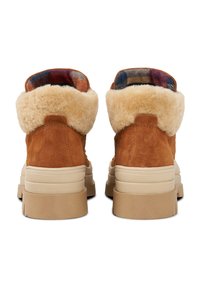 Braune Wildlederstiefel mit einem weichen beigen Pelzkragen und einem gemusterten Innenfutter. Klobige beige Sohle mit strukturierten Akzenten an den Seiten.