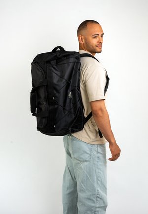 Large black duffel backpack with textured fabric, multiple compartments, and adjustable straps. Features a bungee cord design on the front.