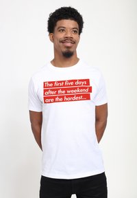 Camiseta de algodón blanca con un bold en rojo que dice: "Los primeros cinco días después del fin de semana son los más difíciles..." en la parte delantera. Mangas cortas.