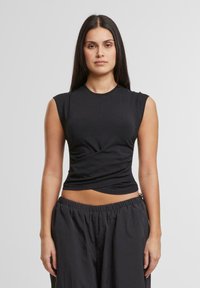 Schwarzes ärmelloses Oberteil aus enganliegendem Stoff, mit rundem Halsausschnitt und gedrehtem Design an der Taille, kombiniert mit lockeren schwarzen Hosen.