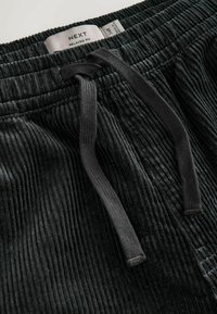 Black corduroy pants with a relaxed fit, featuring a ribbed texture, elastic waistband, and contrasting drawstring. Label visible inside.