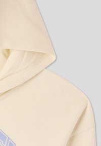 Felpa con cappuccio, di colore crema, materiale in cotone morbido, presenta un cappuccio visibile e dettagli delle cuciture; la texture appare liscia e uniforme.