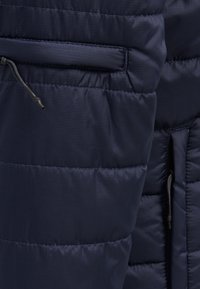 Granatowa kurtka puchowa z pikowanymi panelami, kieszenią na zamek i akcentami z sznurkiem. Wykonana z gładkiego, lekkiego materiału.