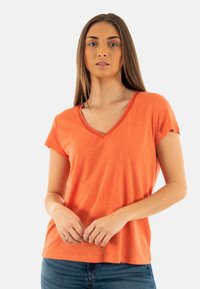 T-shirt en coton orange avec un col en V, manches courtes et coupe décontractée. Présente une texture douce et des coutures visibles le long de l'encolure.