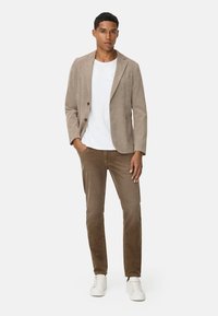 Beige Cordblazer über einem weißen T-Shirt, kombiniert mit braunen Slim-Fit-Hosen und weißen Sneakers. Der Blazer hat zwei Knöpfe und Taschen.