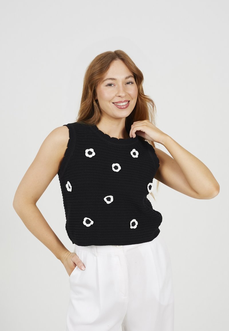 Top senza maniche lavorato a maglia nera con tessuto testurizzato, scollatura scallop e applicazioni bianche a forma di fiore disperse.