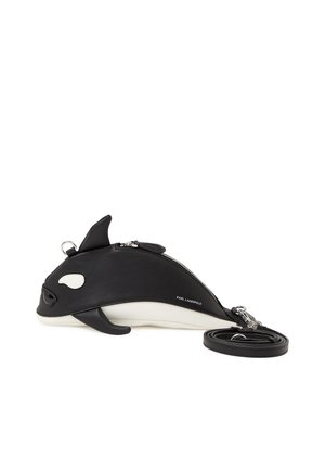 Černobílá kabelka ve tvaru kosatky s uzavíratelným zipem, drobnými detaily ploutve a odnímatelným popruhem navinutým vedle ní.