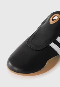 Black leather shoe with white stripes, oval cutout, and a gum sole. Smooth texture with a rounded toe and reinforced stitching.