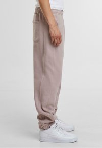 Pantaloni de trening bej deschis, cu talie elastică și manșete, având buzunare laterale și o textură moale, asortați cu adidași albi.