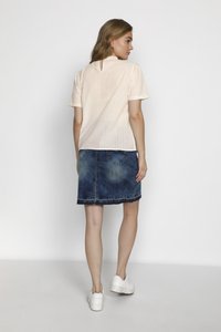 Blusa a strisce pesca chiaro con maniche corte, abbinata a una gonna di jeans blu sbiadito. Sneakers bianche completano l'outfit. Vista posteriore mostrata.
