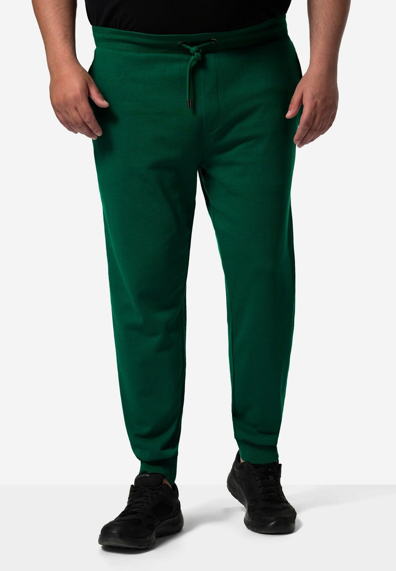Groene sweatpants van zacht materiaal, met een elastische tailleband met een trekkoord, taps toelopende pijpen en zijzakken, gecombineerd met zwarte sneakers.